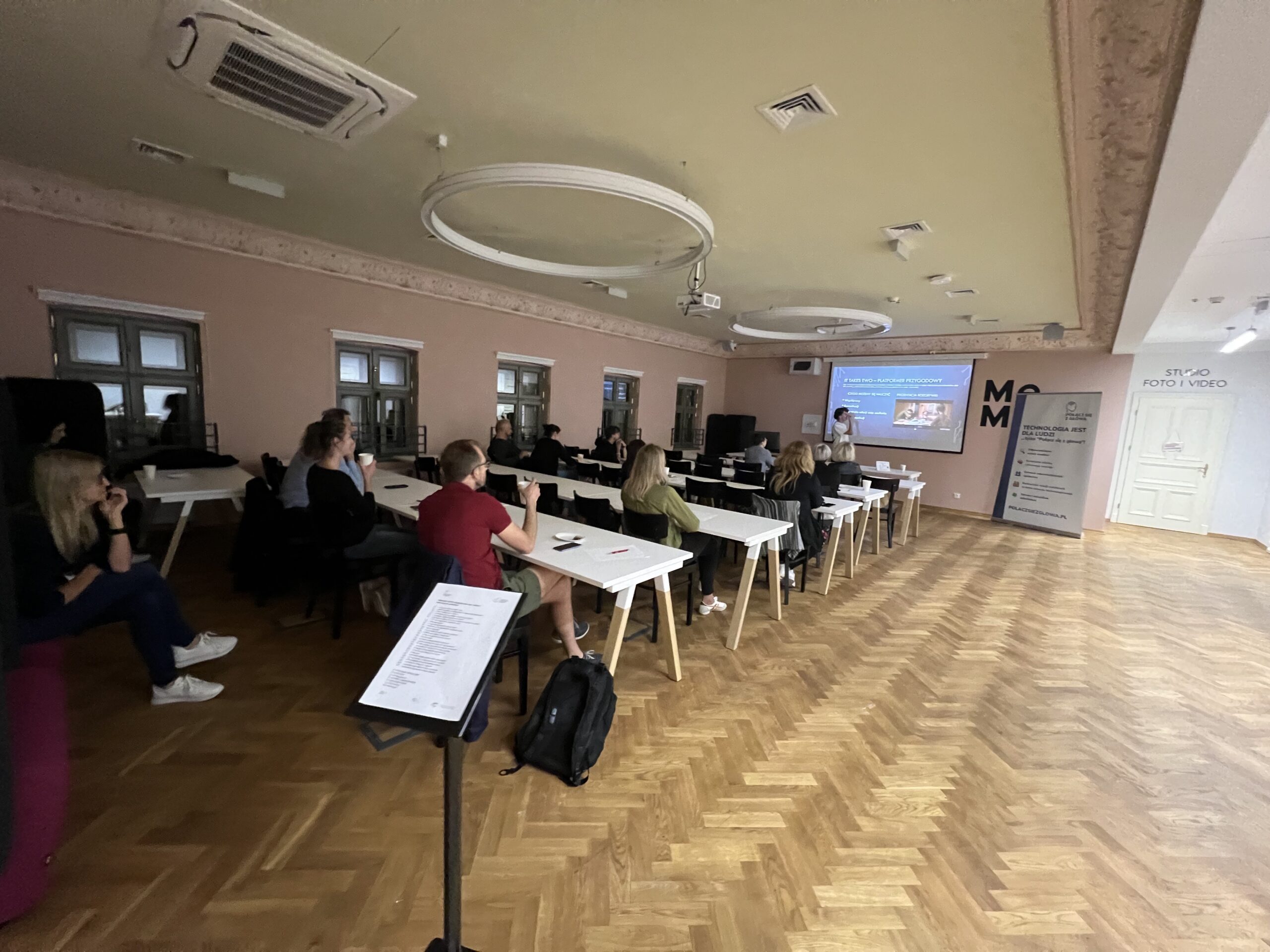 Uczestnicy siedzą na sali i słuchają prezentacji wyświetlanej na ekranie.