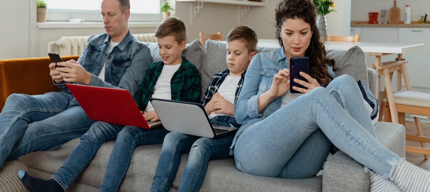 Rodzina siedzi na kanapie, każdy korzysta z własnego urządzenia elektronicznego.