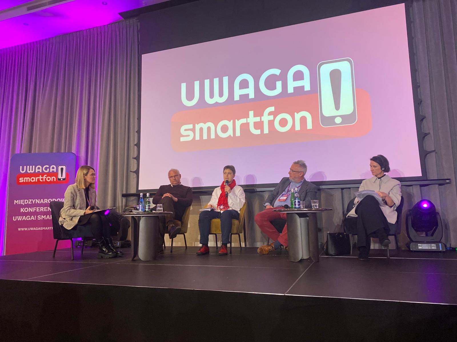 Panel dyskusyjny podczas konferencji „Uwaga Smartfon!”, pięć osób rozmawia na scenie.